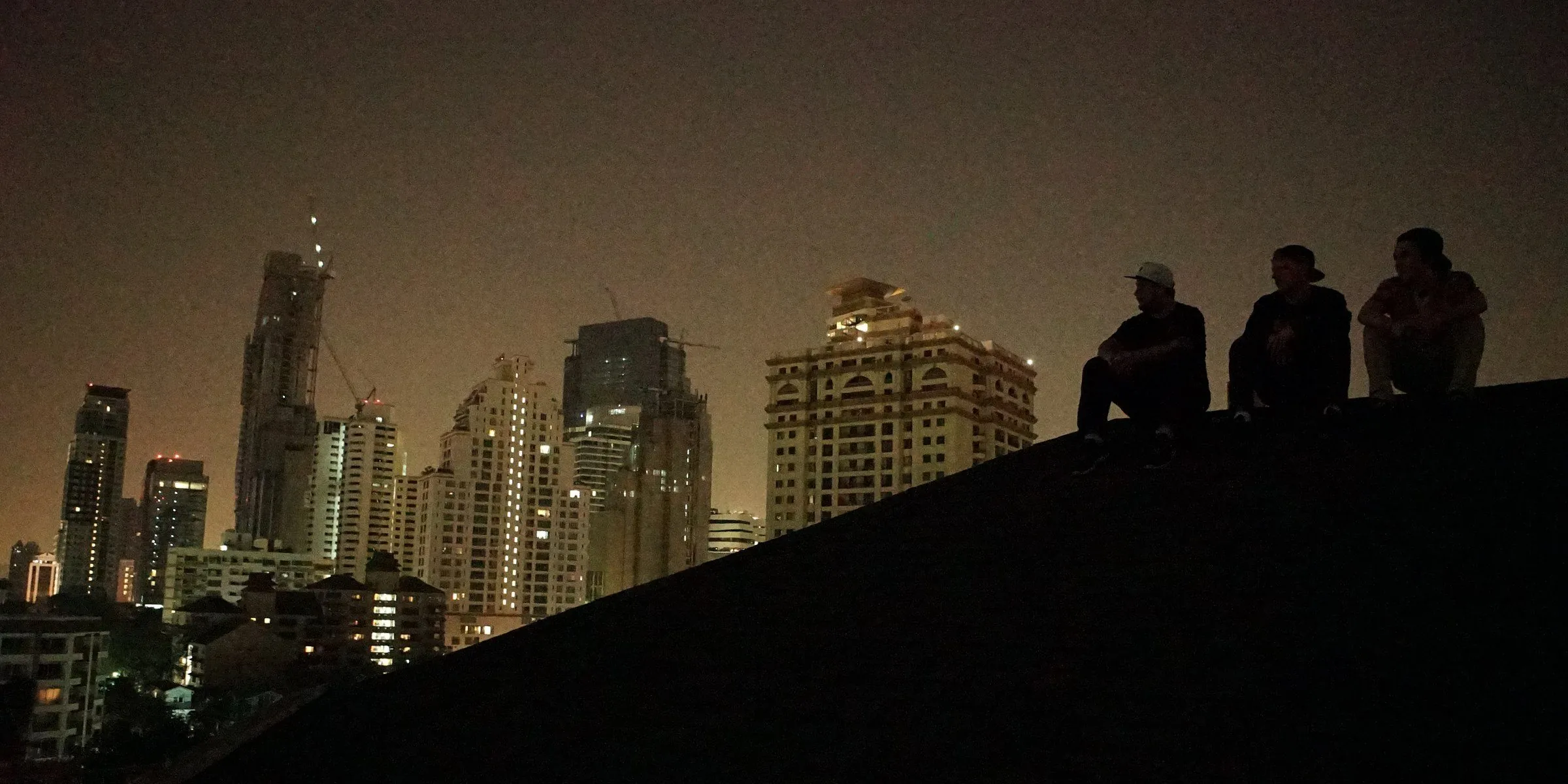 Friends sitting on a rooftop above the city at night